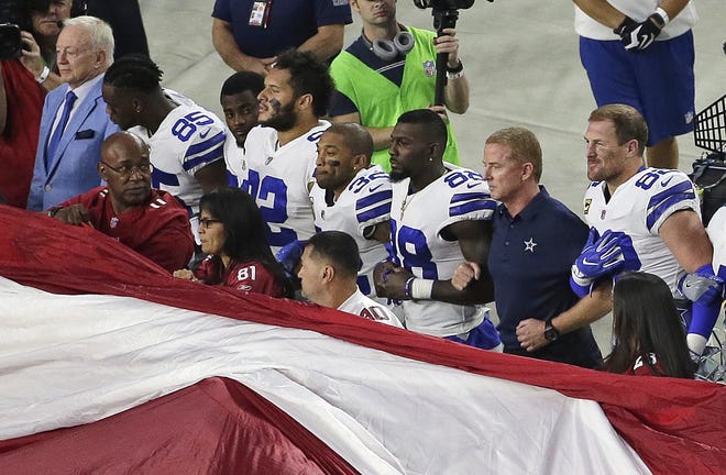 Dallas Cowboys owner Jerry Jones, left, and head coach Jason Garrett, second from right, stand with their players for the national anthem prior to a game against the Arizona Cardinals. [AP File Photo/Matt York]