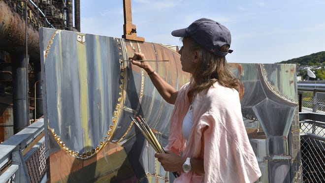In this Sept. 12, 2017 photo, artist Rachel Lussier paints the former Bethlehem Steel plant on the Hoover-Mason Trestle, in Bethlehem, Pa. Unaided by photographs or models, Lussier paints under the elements to try to grab the scope of industry. She's traveled the country, painting B29s and large battleships. Now, she pays homage to the furnaces that fueled the wars. [April Gamiz/The Morning Call via AP]