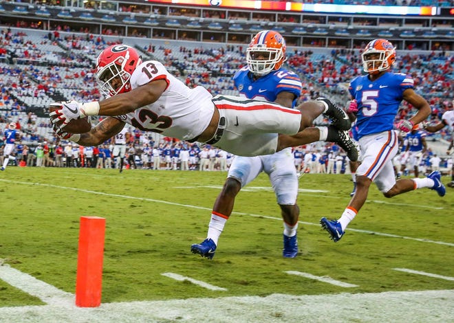Georgia Bulldogs running back Elijah Holyfield (13) dives across the goal line for the Bulldogs’ last touchdown of the day in front of Florida Gators defensive back Chauncey Gardner Jr. (23) and cornerback CJ Henderson (5) at EverBank Field in Jacksonville on Saturday. (For The Florida Times-Union/Gary Lloyd McCullough)