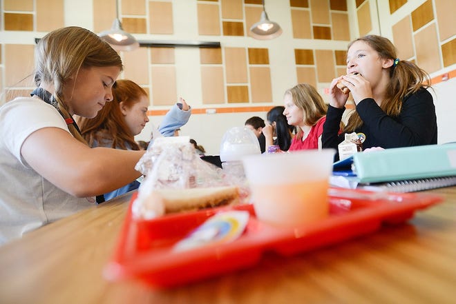 Sophia VanDusen, far right, takes a bite out of a sandwich with classmates during lunch period in the cafeteria on Thursday at New York Mills Union Free School. [ALEX COOPER/OBSERVER-DISPATCH]