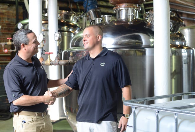 Mark Mullins, Founder and VP of Sales at Social House Vodka, and his brother Jeremiah Mullins, Production Specialist at Social House Vodka, shake hands inside the distillery on Atlantic Avenue. They're both Army Veterans. [Janet S. Carter / The Free Press]