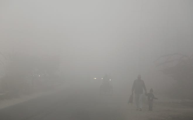 An man and a child emerge from a thick blanket of smog to drop off a child at school on the outskirts of New Delhi Friday. [The Associated Press]