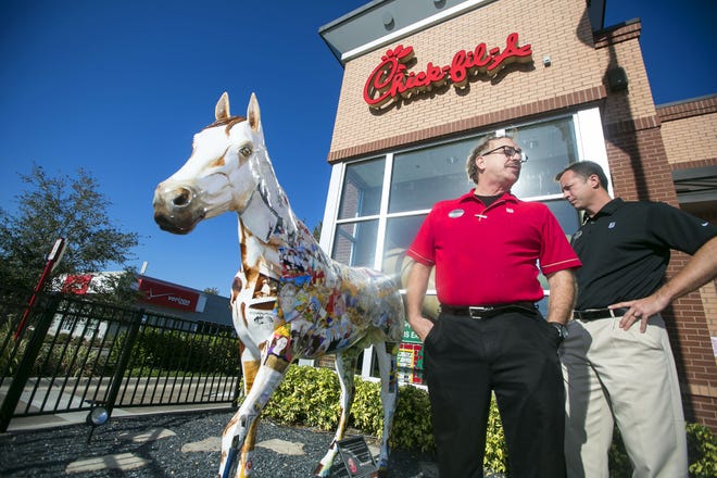 Artist Mark Bushfield, left, and Chick-fil-A owner Jeromy Williams look over the horse Bushfield painted for the restaurant in Ocala. Bushfield, an employee at the eatery, painted a variety of hometown family scenes and other Chick-fil-A related fun all over the statue. A local auto repair shop donated the clear coat sealer to keep it bright. [Alan Youngblood/Staff photographer]