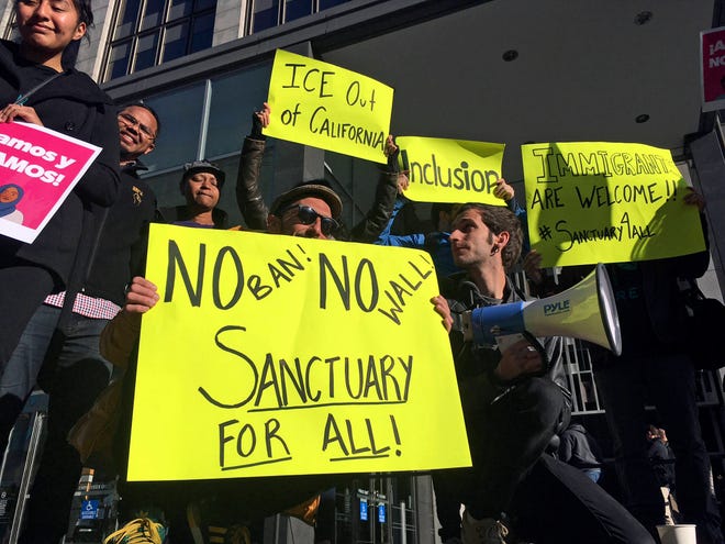 FILE - In this April 14, 2017, file photo, protesters hold up signs outside a courthouse where a federal judge was to hear arguments in the first lawsuit challenging President Donald Trump’s executive order to withhold funding from communities that limit cooperation with immigration authorities in San Francisco. A federal judge Monday, Nov. 20, 2017, has permanently blocked President Donald Trump’s executive order to cut funding from cities that limit cooperation with U.S. immigration authorities. San Francisco and Santa Clara County had filed lawsuits. (AP Photo/Haven Daley, File)
