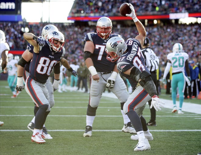 New England Patriots tight end Rob Gronkowski, right, spikes the ball to celebrate his touchdown against the Miami Dolphins with Danny Amendola, left, and Ted Karras, center, during their game Sunday in Foxborough, Mass. [Photo by AP]
