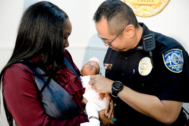 Savannah-Chatham police officer William Eng, right, plays with 29-day-old Bella Adkins while her mother, Tina Adkins, holds her on Monday at Savannah-Chatham police headquarters. Eng performed life-saving CPR on the infant on Friday. (Will Peebles/Savannah Morning News)