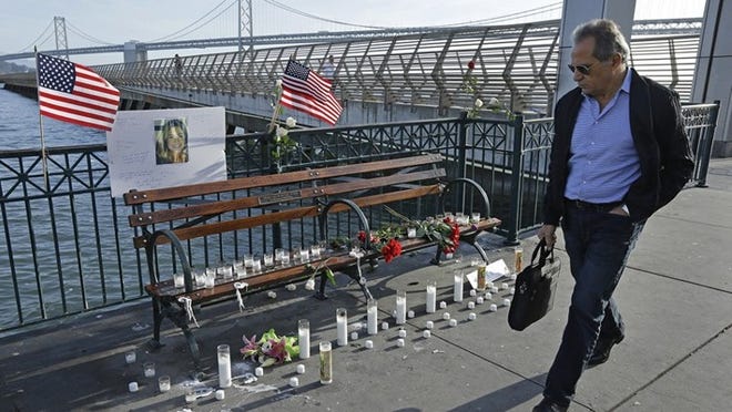 A man walks past candles, flowers, and a photo of Kate Steinle at a memorial site on Pier 14 in San Francisco. (AP Photo/Ben Margot)