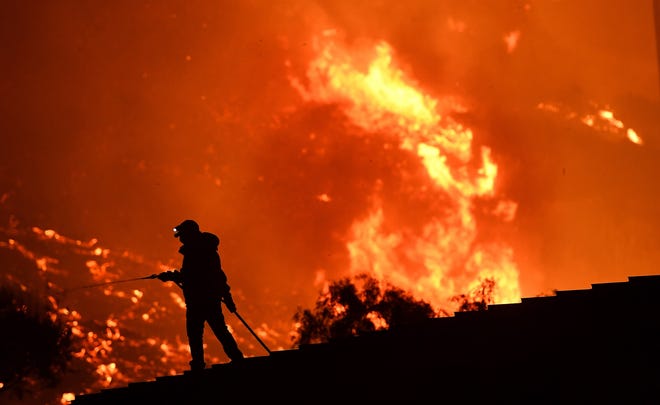 A resident waters a roof as the Thomas Fire approaches the town of La Conchita early Thursday morning. [Wally Skalij / Los Angeles Times/TNS]