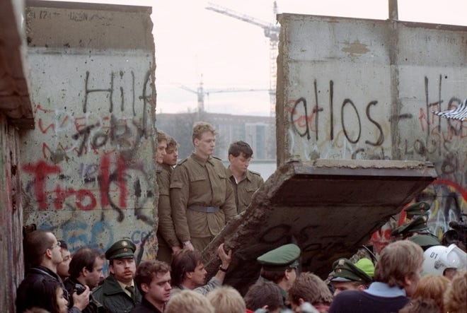 This Nov. 11, 1989 file photo shows East German border guards looking through a hole in the Berlin wall after demonstrators pulled down one segment of the wall at Brandenburg gate. [AP Photo/Lionel Cironneau, File]