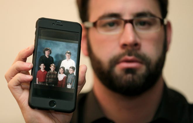 Jamey Anderson holds a photo on his phone of himself, bottom left, at the Word of Faith Christian School with classmates, from left, Liam, Risa Burgeson Pires, and Christopher Davies, and teachers Lisa Brown, top left, and Marty Roper, top right, during an interview in Charlotte, N.C., Monday, Dec. 11, 2017. Throughout his adolescence, Anderson says he was singled out as a rebel and suffered some of the most brutal treatment in the church. Among his transgressions: making a funny face at a classmate. (AP Photo/Chuck Burton)