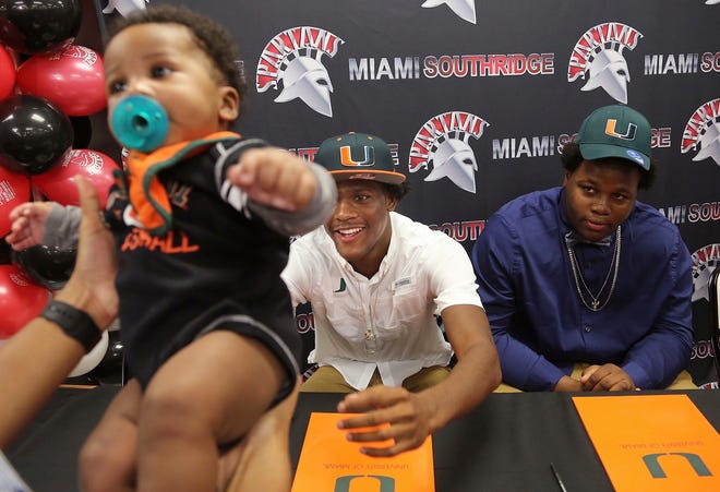 Daquris Wiggins reaches out for his 4 month-old cousin, Sidney August, as teammate Delone Scaife, looks on after the teammates signed with the University of Miami NCAA college football team in Miami, Wednesday, Dec. 20, 2017. (Carl Juste/Miami Herald via AP)