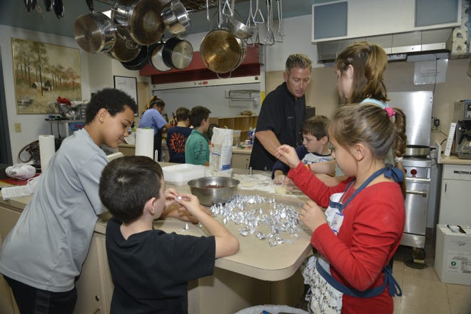 A group of children works on unwrapping Hershey's Kisses as well as shaping dough for doughnuts as Chef Jim Shirah looks on. [SAVANNAH VASQUEZ/THE LOG]