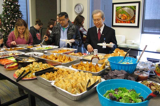 In this Dec. 15, 2017 photo, Tri Phan, right, begins the lunch line for his retirement party at Lutheran Social Services in Fargo, N.D. Phan, 66, spent nearly three decades working in the agency's refugee resettlement program, helping thousands of immigrants from dozens of countries become U.S. citizens. Phan, who was born in Saigon, is moving to California to be closer to his grown children. (AP Photo/Dave Kolpack)