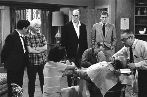 FILE- In this April 11, 1963, file photo, standing from left, Morey Amsterdam, Rose Marie, and Richard Deacon, and Dick Van Dyke, right, gather around Carl Reiner, in barber chair during a rehearsal of an episode for the "The Dick Van Dyke Show." Family spokesman Harlan Boll said Marie, the wisecracking Sally Rogers of “The Dick Van Dyke Show,” died Thursday, Dec. 28, 2017. She was 94. (AP Photo/David F. Smith, File)