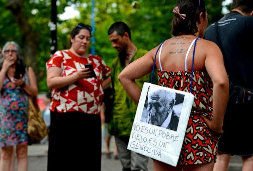 A woman stands with a picture of former police officer Miguel Etchecolatz that reads in Spanish, "He is not a poor man, he is a genocide" during a protest in Mar del Plata, Argentina, Friday, Dec. 29, 2017. Etchecolatz was sentenced to life in prison for crimes against humanity during Argentina last dictatorship but a court in Argentina has granted him house arrest Wednesday, due to health problems. (AP Photo/Marina Devo)