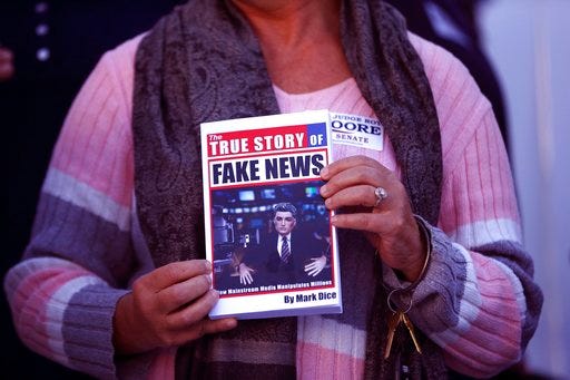 FILE- In a Nov. 17, 2017 file photo, a supporter holds up a "Fake News" book while Kayla Moore, wife of U.S. Senate candidate Roy Moore, speaks at a press conference in Montgomery, Ala. Would a story that seeks to unpack or drill down on a list of tiresome words and phrases be impactful or a nothingburger? Worse, would it just be tons of fake news? Well, dish all you want, but Northern Michigan's Lake Superior State University on Sunday released its 43rd annual List of Words Banished from the Queen's English for Misuse, Overuse and General Uselessness.(AP Photo/Brynn Anderson_File)