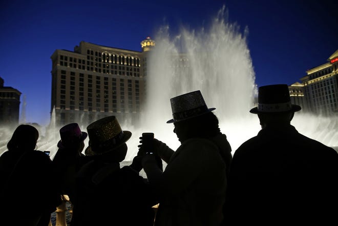 In this Dec. 31, 2015, file photo, people watch the fountains at the Bellagio while wearing paper hats to celebrate New Years Eve in Las Vegas. Tens of thousands of revelers will ring in the New Year in Las Vegas under the close eye of law enforcement just three months after the deadliest mass shooting in modern U.S. history. The Las Vegas Metropolitan Police Department will have every officer working Sunday, Dec. 31, 2017, while the Nevada National Guard is activating about 350 soldiers and airmen. (AP Photo/John Locher, File)