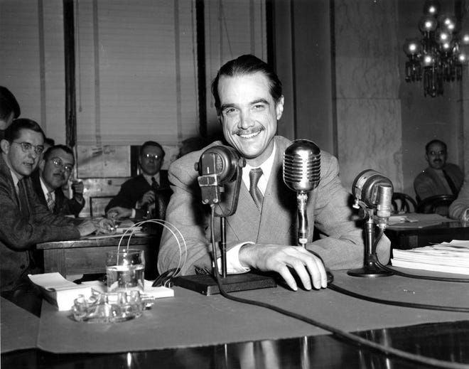 In this Nov. 15, 1947 photo, Howard Hughes smiles as he sits in the witness chair before reading a statement at the Senate War Investigation Subcommittee hearing in Washington, D.C. Four-time and retired NASCAR champion Jeff Gordon was an obvious choice for the Motorsports Hall of Fame. (AP Photo/File)