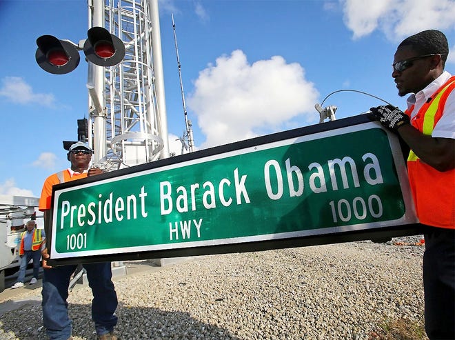 In this Dec. 17, 2015 file photo, Dale Moncur, left, and Cedric Anderson of Palm Beach County Traffic Operations, hold a sign for the new President Barack Obama Highway in preparation to change it from the “Old Dixie Highway” in Riviera Beach, Fla. On Friday, The Associated Press reported that stories circulating on the internet about President Donald Trump ordering the name of the highway changed back to “Old Dixie” are untrue. [LANNIS WATERS/PALM BEACH POST/ASSOCIATED PRESS]