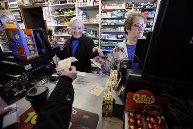 Cashiers Kathy Robinson, left, and Ethel Kroska, right, both of Merrimack, N.H., sell a lottery ticket Sunday, Jan. 7, 2018, to Diane Ackley, hand only below, at Reeds Ferry Market convenience store, in Merrimack. A lone Powerball ticket sold at Reeds Ferry Market matched all six numbers and will claim a $559.7 million jackpot. [AP Photo/Steven Senne]