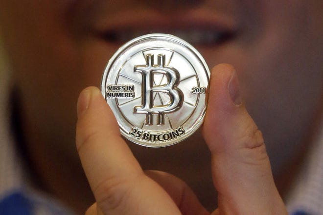 In this April 3, 2013 photo, Mike Caldwell, a 35-year-old software engineer, holds a 25 Bitcoin token at his shop in Sandy, Utah. Bitcoin is an online currency that allows people to make one-to-one transactions, buy goods and services and exchange money across borders without involving banks, credit card issuers or other third parties. (AP Photo/Rick Bowmer)