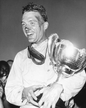 This 1962 photo shows Dan Gurney holding a trophy in Nassau, Bahamas. Gurney, the first driver to win in Formula One, IndyCar and NASCAR, died Sunday. (Associated Press File)