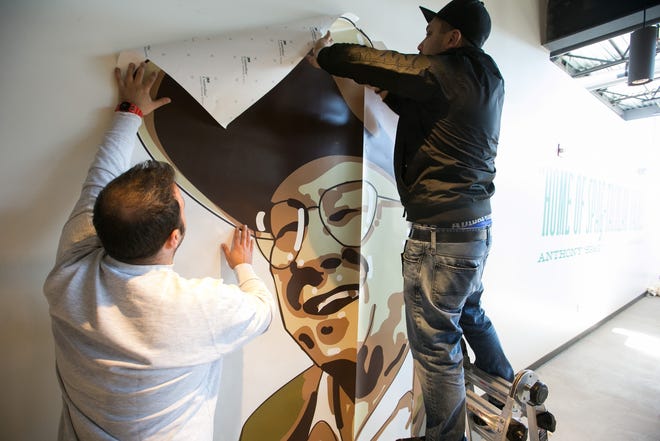 Al Tamer, left, and Kevin Tamer of DGI Invisuals hang a wall mural featuring Anthony "Spag" Borgatti inside the Whole Foods in Shrewsbury on Thursday. The store is set to open Jan. 30 and pays homage Spags throughout the building. [Photo/Matthew Healey]