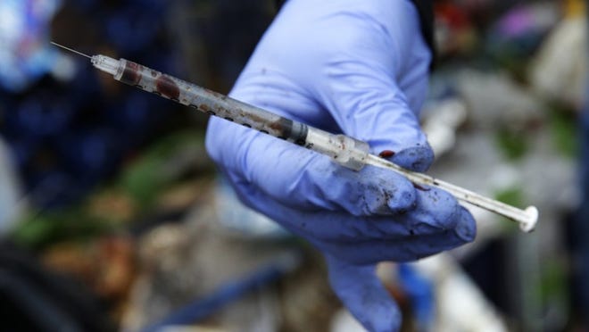 Volunteer outreach worker with The Hand Up Project, an addiction and homeless advocacy group, holds a used and blood-filled needle used for drug injection fount at a homeless encampment in Everett, Wash. (AP Photo/Ted S. Warren, File)