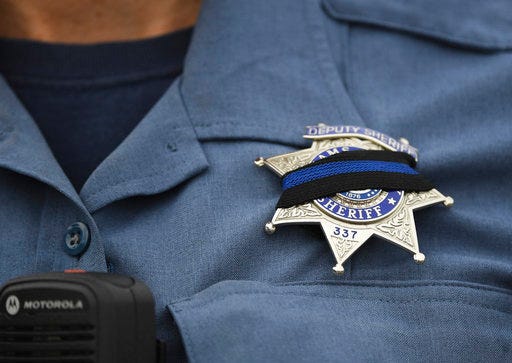 An Adams County Sheriff Deputy wears a black band across her badge after Sheriff's Deputy Heath Gumm was gunned down, Thursday, Jan. 25, 2018 in Thornton, Colo. Authorities in Colorado have arrested one man and are searching for two other suspects in connection with the killing of Gumm, a sheriff's deputy, leading some schools in the area to shut down. (RJ Sangosti/The Denver Post via AP)