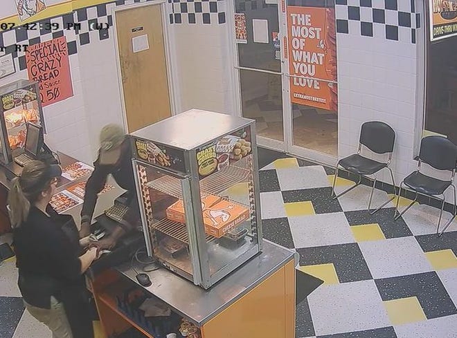 A man reaches over the counter at the Holly Hill Little Caesar's restaurant and grabs cash from the register. Police believe the same person robbed a Little Caesar's in Edgewater. [Holly Hill Police Department]