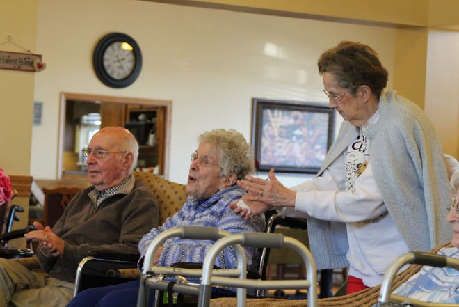 Marilyn Lloyd, a former elementary school and music teacher, encourages Joan and Keith Foley to clap along Monday to music performed by juniors in the Notre Dame High School choir at Bickford Senior Living. [Michaele Niehaus/thehawkeye.com]