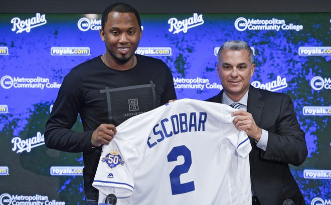Kansas City Royals' Alcides Escobar, left, holds his jersey next to general manager Dayton Moore after re-signing with the team, during a news conference Monday at Kauffman Stadium in Kansas City, Mo. [John Sleezer, The Kansas City Star/Associated Press]