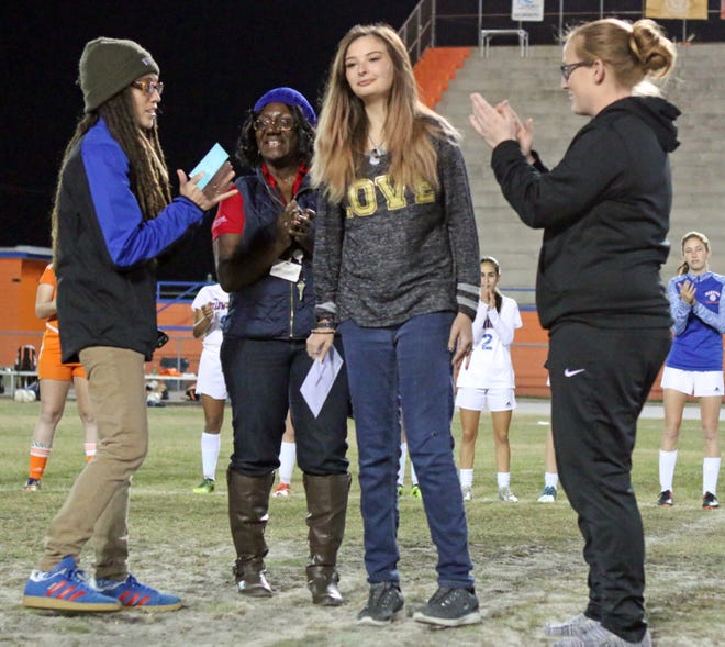 From left, Bartow coach Eina Dorado, Kathleen teacher Marina Peters-Green and Kathleen coach Kristin Nicholson, far right, applaud after Kathleen soccer player Kendra Gilleland received a check for $1,000 from Bartow family and friends, prior to a district soccer game last week. [ROY FUOCO/THE LEDGER]