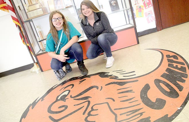 Jonesville Middle School sixth-grader Lyra Nichols and eighth-grader Olivia Johnson pose for a picture in front of the Comet logo at the school. The girls along with seventh-grader Kenadi Rundquist recently raised money for the Greater Hillsdale Humane Society. [ANDY BARRAND PHOTO]