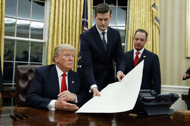 White House Staff Secretary Rob Porter hands President Donald Trump a confirmation order Jan. 20, 2017, in the Oval Office, as White House Chief of Staff Reince Priebus watches. Porter and speechwriter David Sorenson have both stepped down following allegations of domestic abuse. [Evan Vucci/The Associated Press]