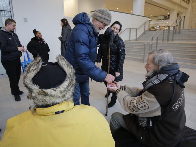 Volunteers Mike Hock and Stacie Klein, middle, with Harmony Project, hand out "kindess packs" of COTA day passes and Roots Cafe meal vouchers to Tony Jarrett, left, and John Albrech at the main branch of the Columbus Metropolitan Library Downtown. [Tom Dodge/Dispatch]