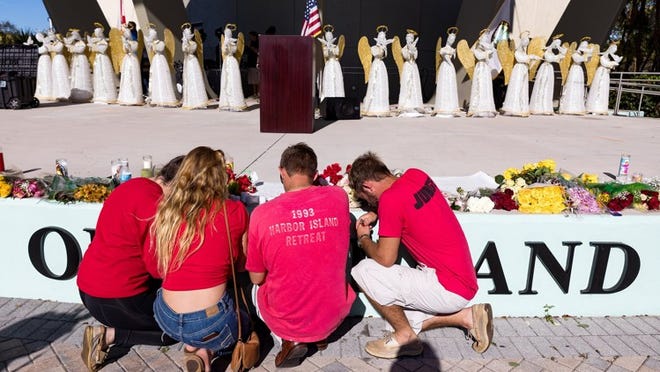 People kneel on the stage where flowers and 17 angels stand before a memorial service Thursday for the victims of the shooting at Marjory Stoneman Douglas High School that killed 17 people. (Greg Lovett / The Palm Beach Post)