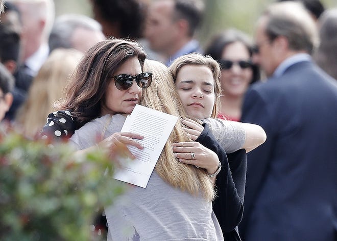 Mourners hug as they leave the funeral of Alaina Petty, in Coral Springs, Fla., Monday. Petty was a victim of Wednesday's mass shooting at Marjory Stoneman Douglas High School. Nikolas Cruz, a former student, was charged with 17 counts of premeditated murder on Thursday. [GERALD HERBERT/ASSOCIATED PRESS]