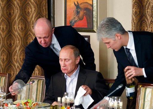 FILE - In this Friday, Nov. 11, 2011 file photo, businessman Yevgeny Prigozhin, left, serves food to Russian Prime Minister Vladimir Putin, center, during dinner at Prigozhin's restaurant outside Moscow, Russia. Ten years ago, he served plates to President Vladimir Putin. These days, St. Petersburg-based businessman Yevgeny Prigozhin funds Kremlin trolls and sends mercenaries to help Russia's military operation in Syria _ all with one aim: to do the president favors that would be too risky for other Russian moguls to undertake. (AP Photo/Misha Japaridze, Pool, File)