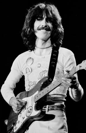 FILE - In this 1974 file photo, George Harrison performs in a concert in Landover, Md. Paul McCartney and George Harrison's widow and son have publicly remembered the late Beatle on what would have been his 75th birthday. (AP Photo/Bob Grieser, File)