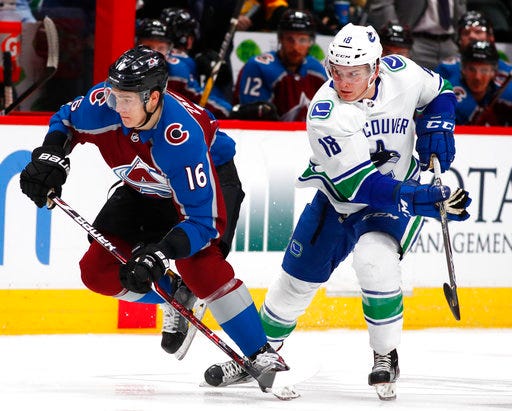 Colorado Avalanche defenseman Nikita Zadorov, left, races to pick up the loose puck with Vancouver Canucks right wing Jake Virtanen in the second period of an NHL hockey game Monday, Feb. 26, 2018, in Denver. (AP Photo/David Zalubowski)