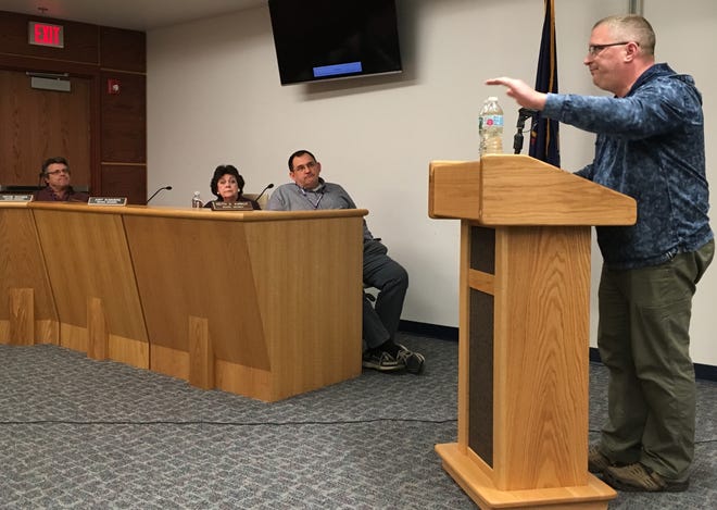 Paul Fazio (right), the parent of a Resica Elementary student, shows a sample of amber-colored water taken from his daughter’s school. East Stroudsburg school board members (from left to right) Wayne Rohner, Judy Summers and Keith Karkut watch as Fazio compares the sample to a bottle of clear water during Monday's public meeting. [Bill Cameron/Pocono Record]