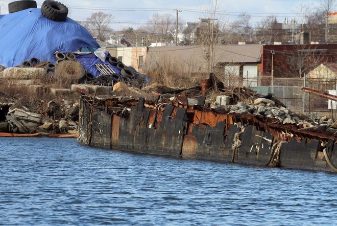 The scene in late December at R.I. Recycled Metals on Allens Avenue, Providence. In the foreground is the half-demolished hull of the Russian submarine Juliett 484, and in the background, covered by blue tarps, soil that the business dug from the riverbank on a site of previous industrial contamination to create a "graving dock" where it could haul out vessels and break them into scrap. [The Providence Journal / Bob Breidenbach]