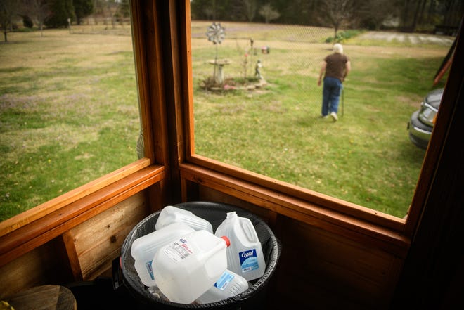 Empty water jugs sit in a trash can as Merle Stevens walks out to her garden in Cumberland County. She and her husband John no longer use their well water, except for bathing, and will no longer eat anything from their garden because of GenX from the Chemours plant. [Andrew Craft/The Fayetteville Observer]
