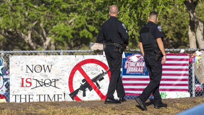 Police walk past memorials on the fence in front of Marjory Stoneman Douglas High School on Wednesday morning. (Lannis Waters / The Palm Beach Post)
