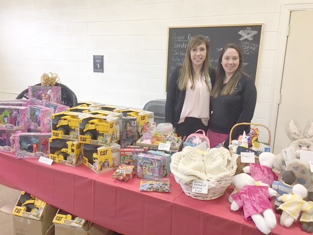 Lindsay Deering, a representative from C.S. Mott Children’s Hospital and Ashley Oteney stand behind a table filled with toys to be donated to the hospital. [COURTESY PHOTO]