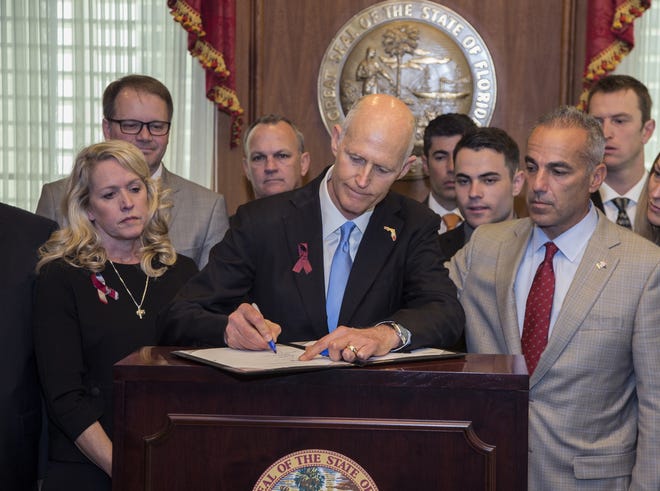 Florida Gov. Rick Scott signs the Marjory Stoneman Douglas Public Safety Act in the governor's office at the Florida State Capitol in Tallahassee on Friday. Scott is flanked by victims' parents Gena Hoyer, left, Ryan Petty, second from left, Andrew Pollack, right, and his son Hunter Pollack, second from right. [ASSOCIATED PRESS/MARK WALLHEISER]