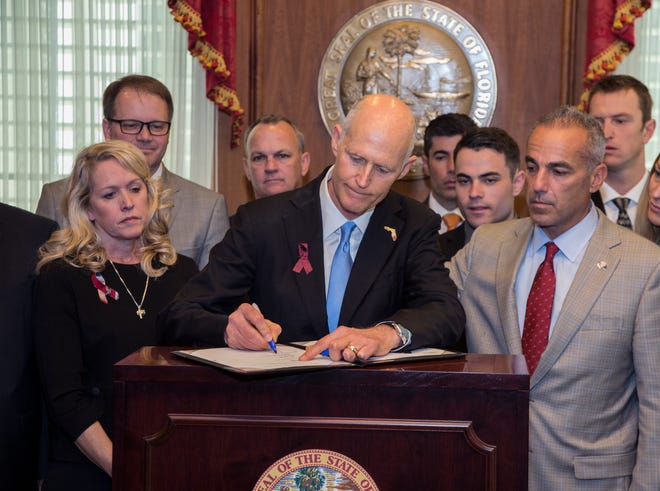 Florida Gov. Rick Scott signs the Marjory Stoneman Douglas Public Safety Act in the governor's office at the Florida State Capitol in Tallahassee on Friday. Scott is flanked by victims' parents Jennifer Montalto, left, Ryan Petty, second from left, Andrew Pollack, right, and his son Hunter Pollack, second from right. [AP Photo / Mark Wallheiser]