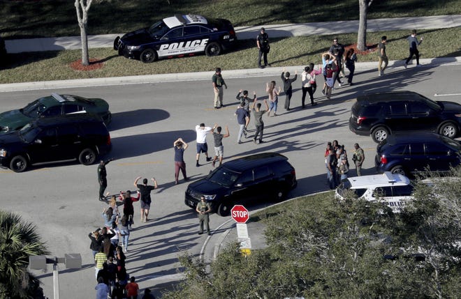 Students hold their hands in the air as they are evacuated by police from Marjory Stoneman Douglas High School on Feb. 14 in Parkland, after a shooter opened fire on the campus. Emergency calls from parents and students during the Florida high school massacre show 911 operators at first trying to grasp the enormity of the emergency and then calmly trying to gather information to assist arriving law enforcement officers. The officers arrive to find chaos as delays allowed the shooter to flee. [Mike Stocker/South Florida Sun-Sentinel via AP]