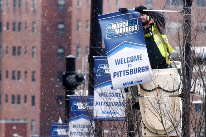 Khalid Karri, with Airborne Promotions, unrolls a banner for the NCAA college basketball tournament to hang along Centre Avenue in front of the PPG Paints Arena, Friday March 9, 2018, in Pittsburgh, The arena hosts the March 15 and March 17 first and second rounds games. (Darrell Sapp/Pittsburgh Post-Gazette via AP)